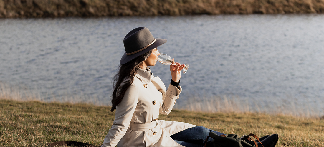 Lady drinking sparkling on grass overlooking the water
